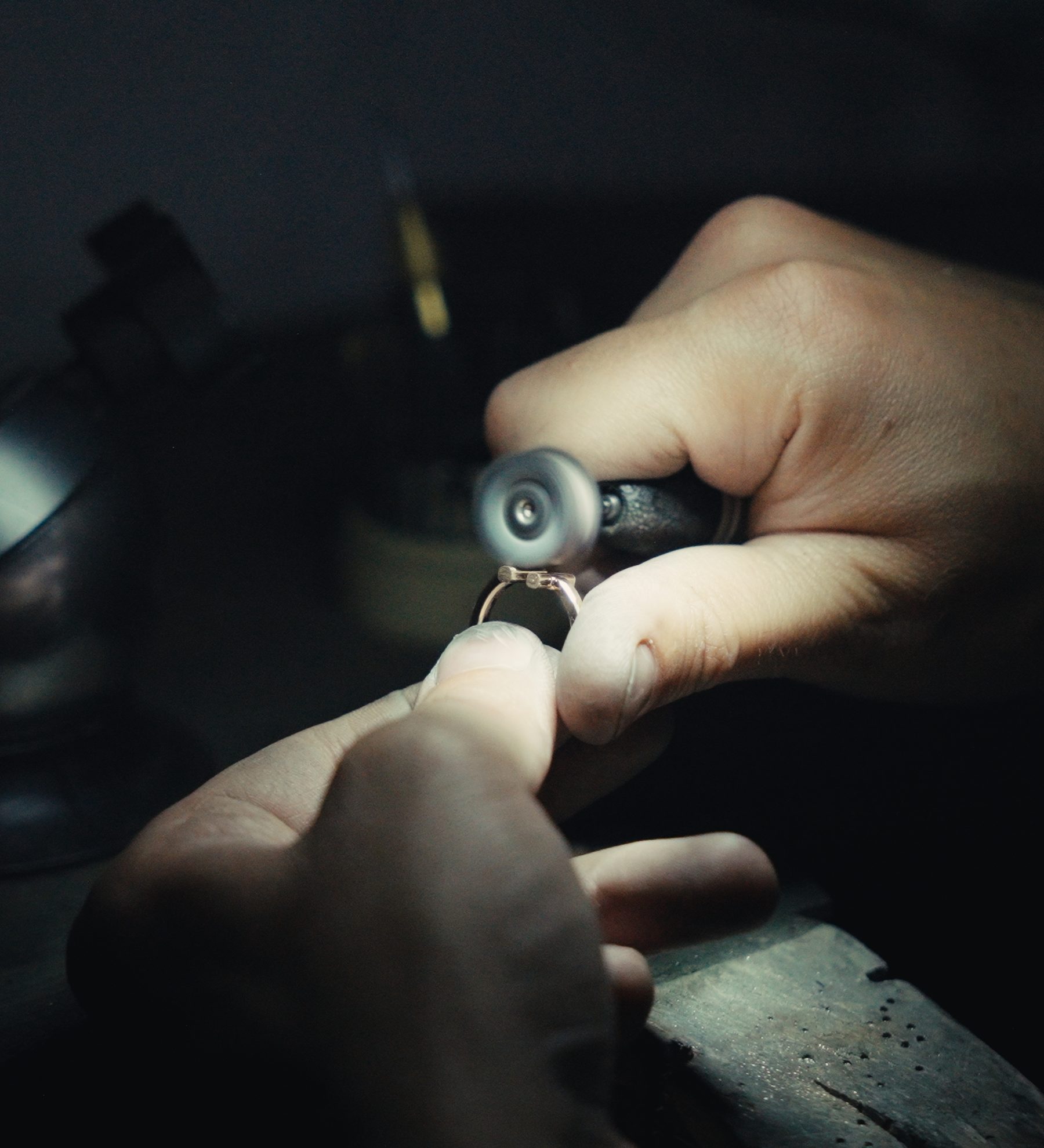 A goldsmith holding a ring under a loupe at the bench